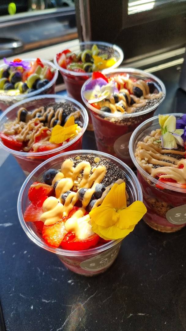 Several clear plastic cups filled with smoothie bowls topped with fruit, nuts, and edible flowers