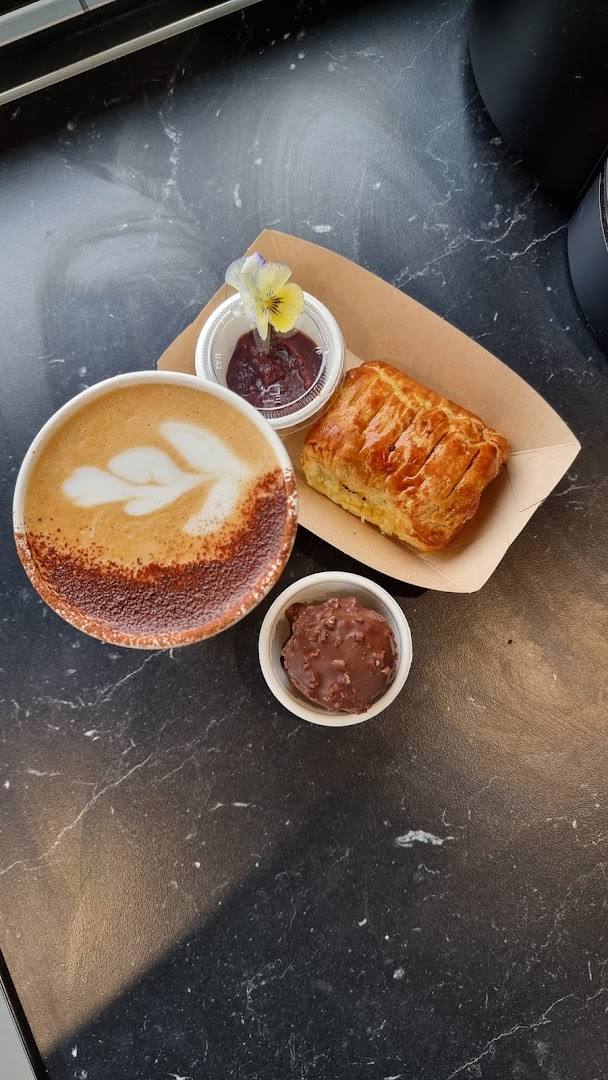 Coffee with latte art, pastry, jam, and chocolate treat on a counter
