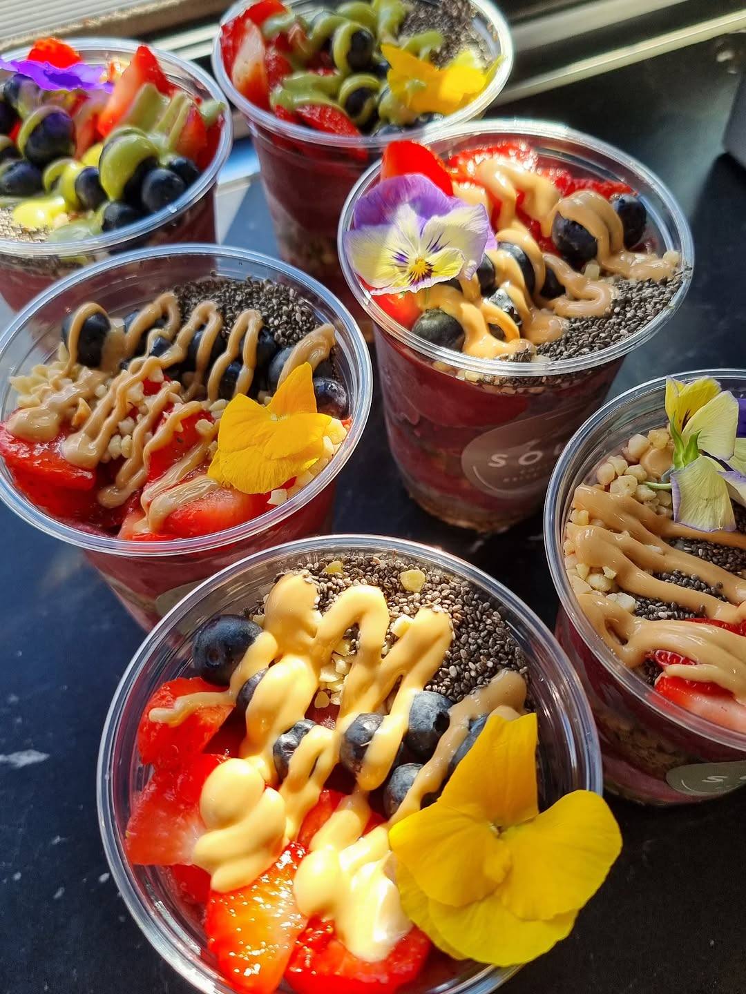 Several acai bowls topped with fruit, nuts, seeds, and edible flowers