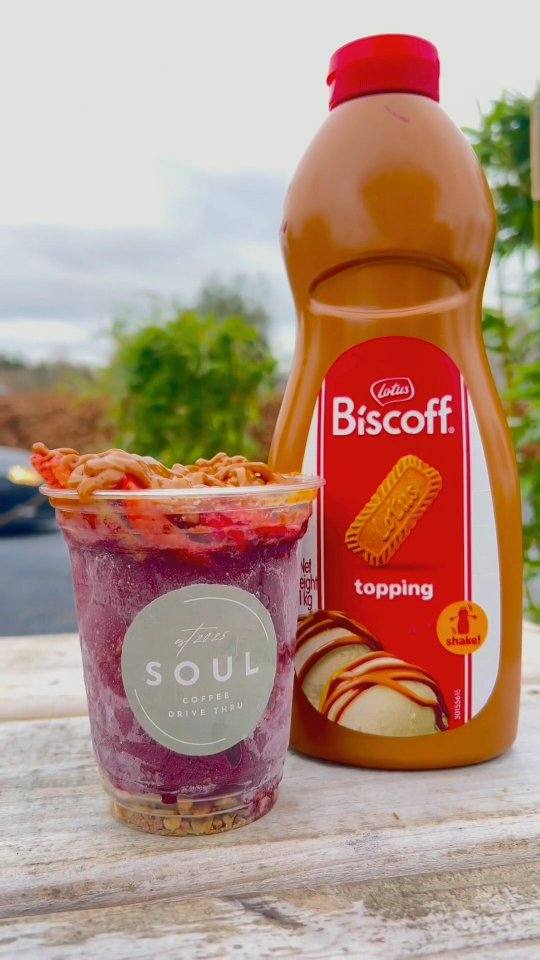 Acai cup with Biscoff drizzle next to a bottle of Lotus Biscoff topping