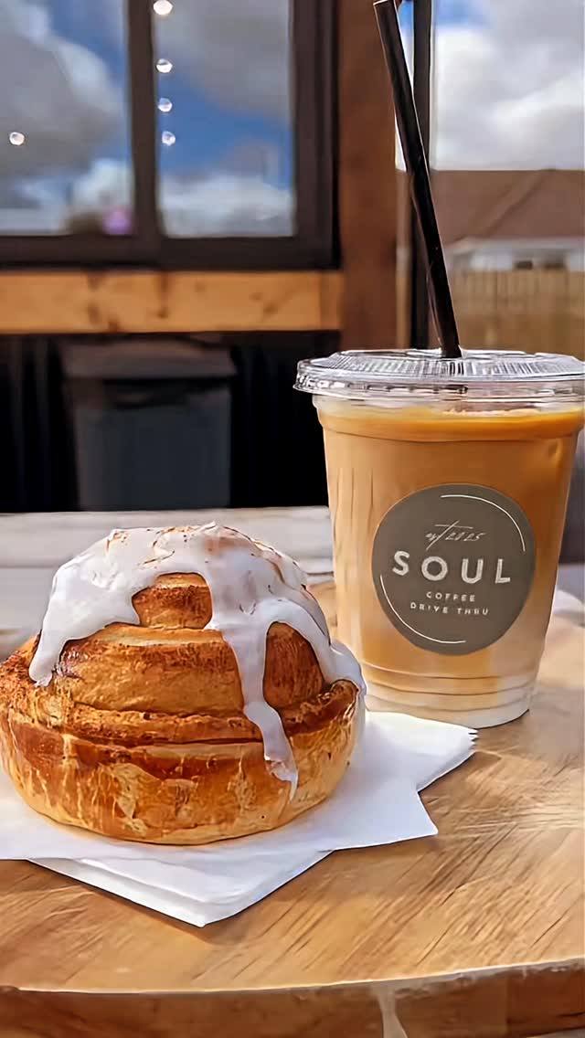 Iced coffee in a branded plastic cup and a frosted cinnamon roll on a wooden table