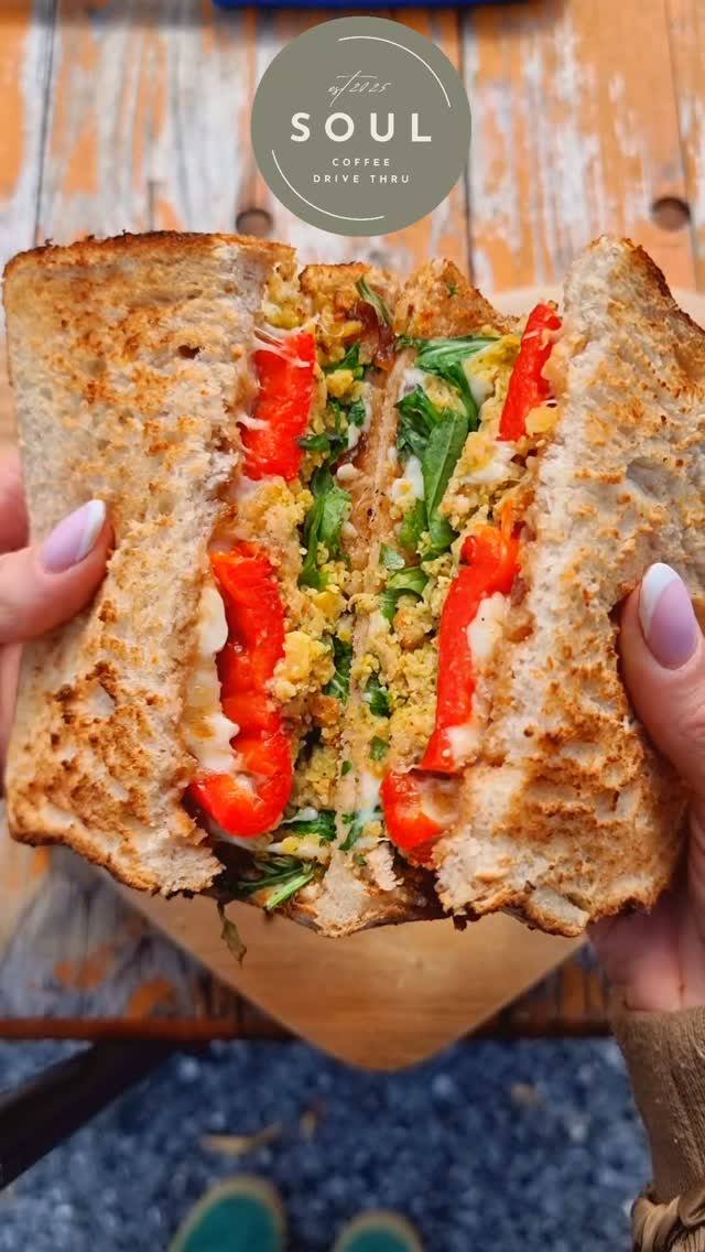 A toasted sandwich cut in half filled with red peppers, greens, and melted cheese