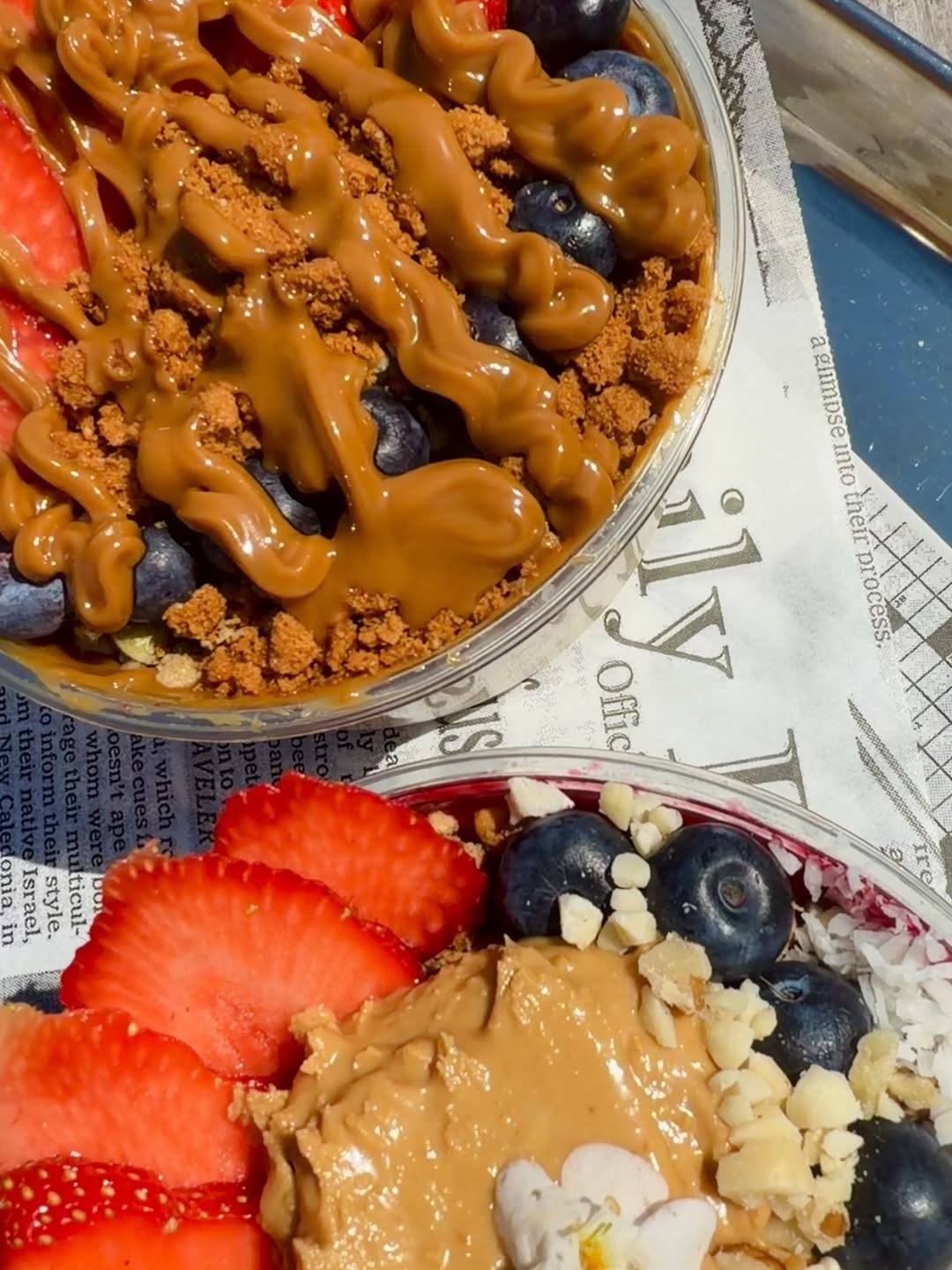 Two acai bowls topped with strawberries, blueberries, and a rich drizzle